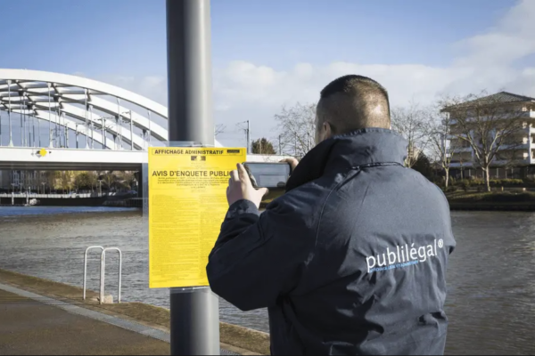 Riverain photographiant un avis d'enquête publique affiché en zone urbaine