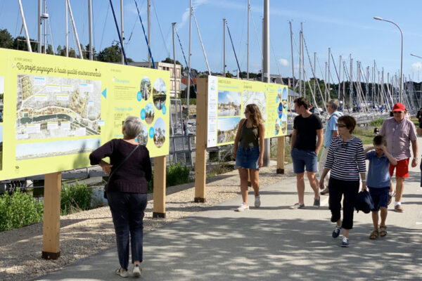 Visiteurs consultant des panneaux d'exposition sur un projet d'aménagement paysager le long d'un port de plaisance