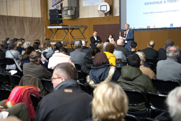Salle de réunion publique remplie, public attentif à une présentation projetée