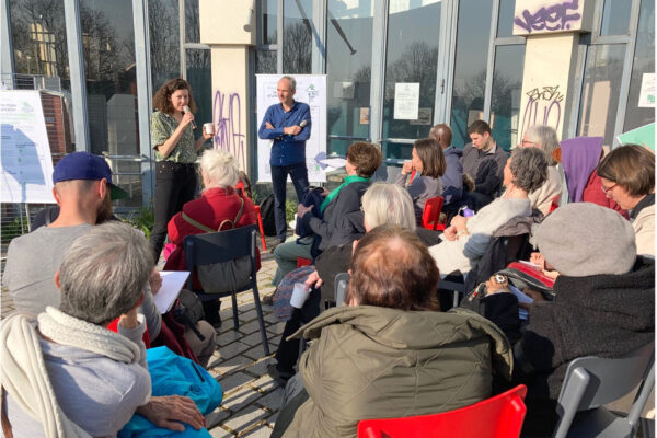 Réunion publique en salle, animateur debout face à des habitants assis en cercle